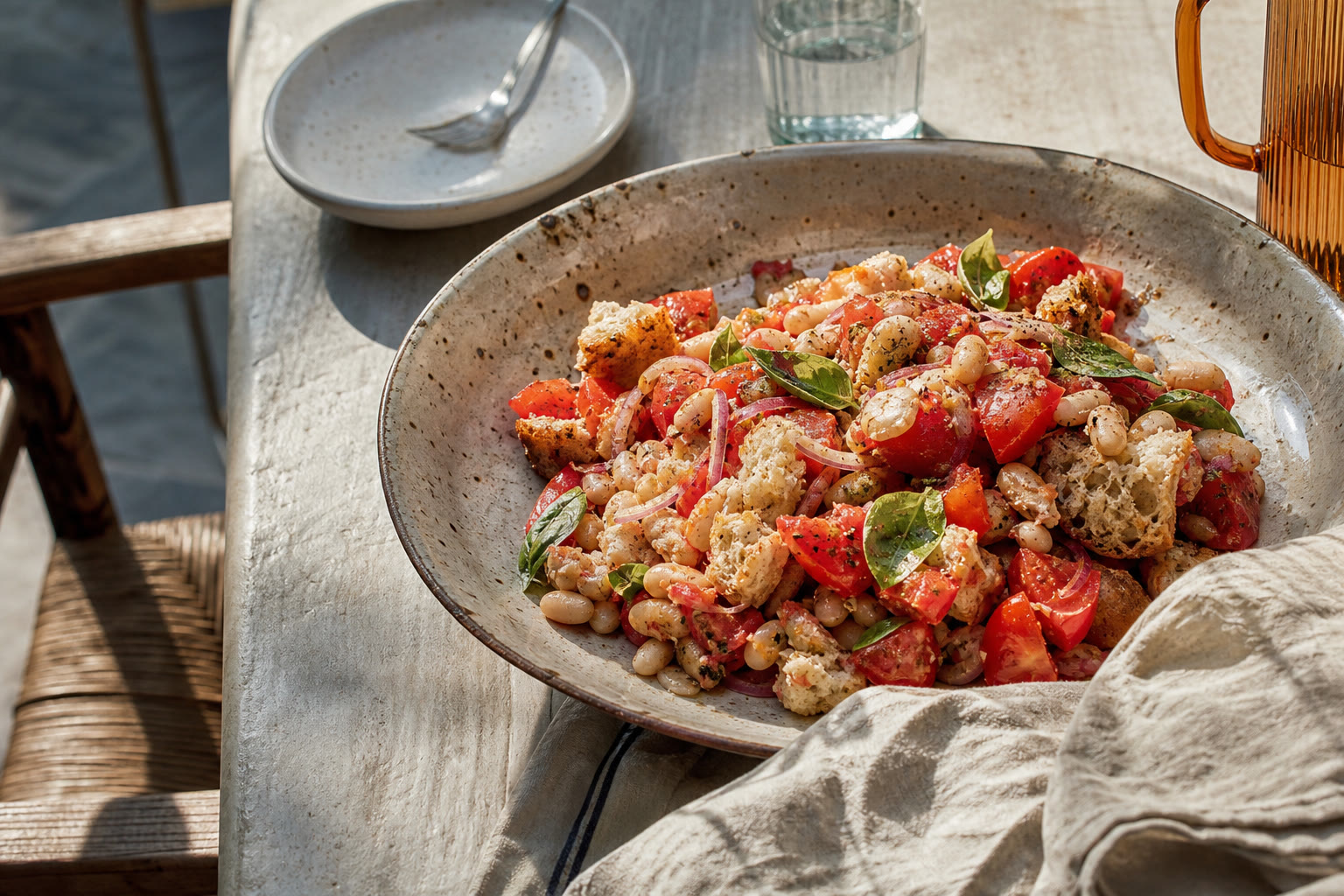 Panzanella in un grande piatto di ceramica artigianale: pane, pomodori maturi, cannellini, basilico e cipolla sottile su un tavolo estivo italiano